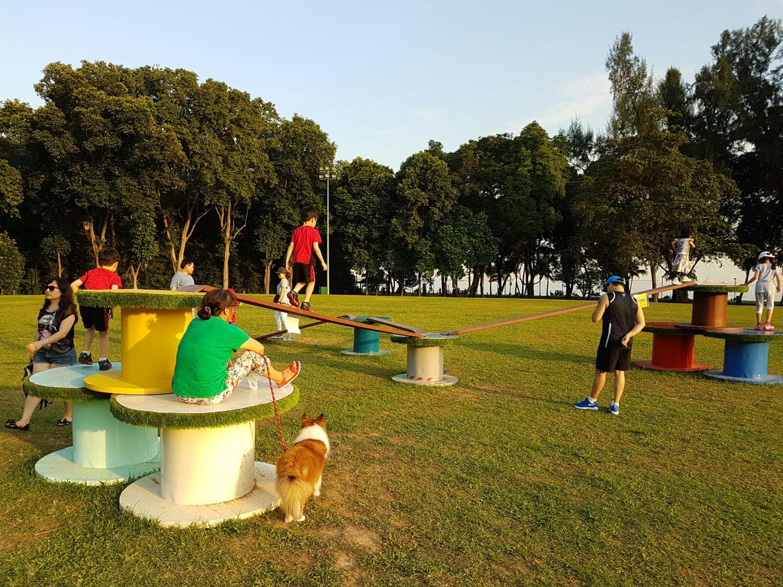 Children playing on unique playground equipment on a grassy field with trees in the background.